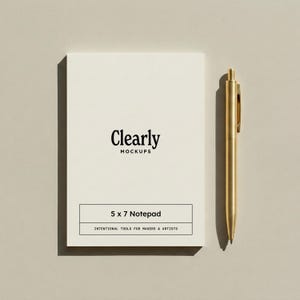 Puede incluir: Un bloc de notas blanco de 5 x 7 pulgadas con el texto "Clearly Mockups" y "Intentional Tools for Makers & Artists". Un bolígrafo dorado descansa junto al bloc de notas. El bloc de notas y el bolígrafo están sobre un fondo neutro.