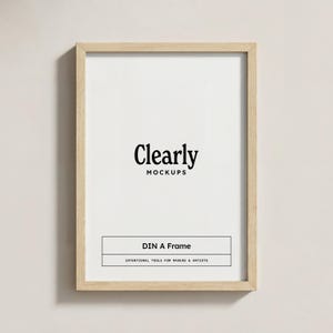 Könnte beinhalten: Ein rechteckiger, hellfarbiger Holzrahmen mit weißem Innenraum. Der Text "Clearly MOCKUPS" ist oben zentriert, darunter "DIN A Frame" und "INTENTIONAL TOOLS FOR MAKERS & ARTISTS". Der Rahmen wird vor einem neutralen Hintergrund angezeigt.