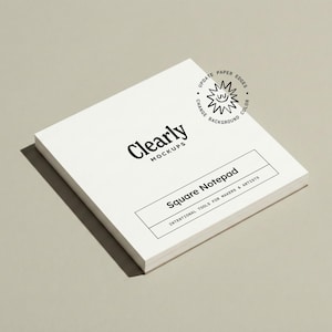 May include: A square white notepad with the text "Clearly Mockups" and "Square Notepad". The notepad has a clean, minimalist design, with a shadow on a neutral background. The text "Intentional Tools for Makers & Artists" is also visible.