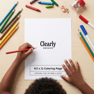 May include: A person's hands holding a red pencil over an 8.5 x 11 inch coloring page. The page is surrounded by various colored pencils, crayons, and a pencil sharpener. The page has the text "Clearly Mockups" and "8.5 x 11 Coloring Page".