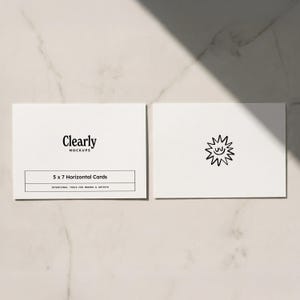 Puede incluir: Dos tarjetas horizontales blancas de 12,7 x 17,8 cm. Una tarjeta tiene el texto "Clearly Mockups" y "5 x 7 Horizontal Cards". La otra tarjeta tiene un dibujo lineal negro de un sol sonriente. Las tarjetas están sobre una superficie clara.