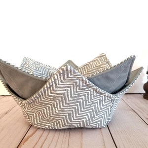 May include: A gray and white chevron patterned fabric bowl. The bowl is folded and has a gray fabric lining.