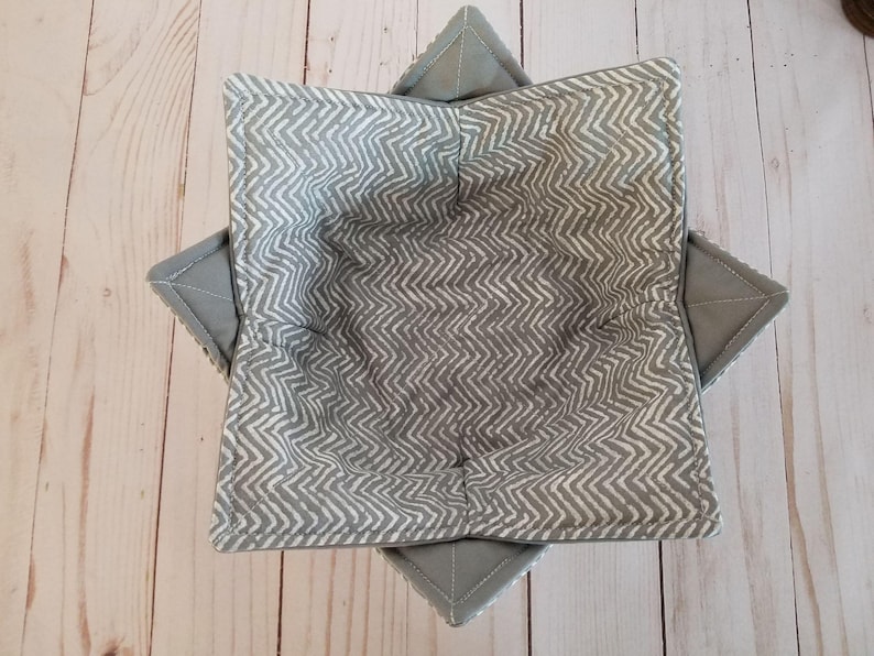 K&ouml;nnte beinhalten: Eine graue Stoffsch&uuml;ssel mit einem wei&szlig;en Zickzackmuster. Die Sch&uuml;ssel ist zusammengefaltet und bereit zum Gebrauch.
