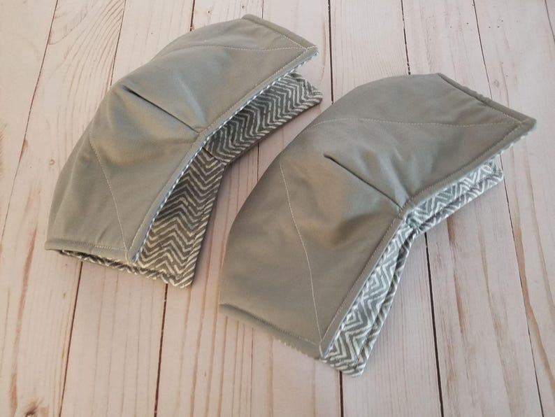 K&ouml;nnte beinhalten: Zwei graue Topflappen aus Stoff mit einem wei&szlig;en und grauen Zickzackmuster. Die Topflappen sind aus weichem, gestepptem Stoff.