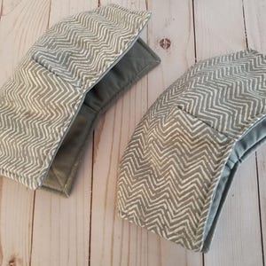 K&ouml;nnte beinhalten: Zwei graue und wei&szlig;e Sch&uuml;sselw&auml;rmer aus Stoff mit Chevron-Muster. Die W&auml;rmer sind aus weichem, gestepptem Stoff gefertigt und haben ein graues Futter.