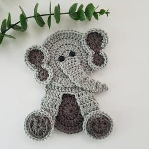 May include: A handmade crochet elephant in shades of gray and dark gray. The elephant has large ears, a trunk, and small black eyes. The crochet animal is a cute, whimsical design.