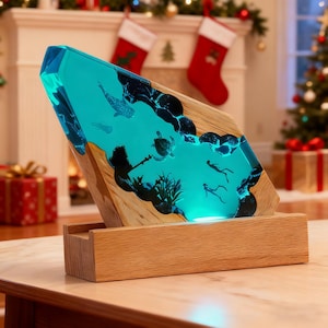 May include: A decorative wooden lamp with a turquoise resin center, featuring an underwater scene with fish, turtles, and divers. The lamp sits on a wooden base and is illuminated with a soft blue light. The lamp is approximately 12 inches tall.