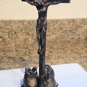 May include: A dark bronze crucifix sculpture featuring a figure of Jesus Christ on the cross. The base of the sculpture has a decorative design. The sculpture is made of a dark bronze material.