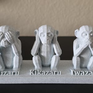May include: A light grey sculpture of the three wise monkeys. One covers its eyes, one its ears, and the last its mouth. The base has the words "Mizaru", "Kikazaru", and "Iwazaru".