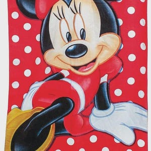 May include: A red and white polka dot beach towel featuring a smiling Minnie Mouse. Minnie is wearing a red dress, bow, and gloves. The towel has the text "It's all about Me".