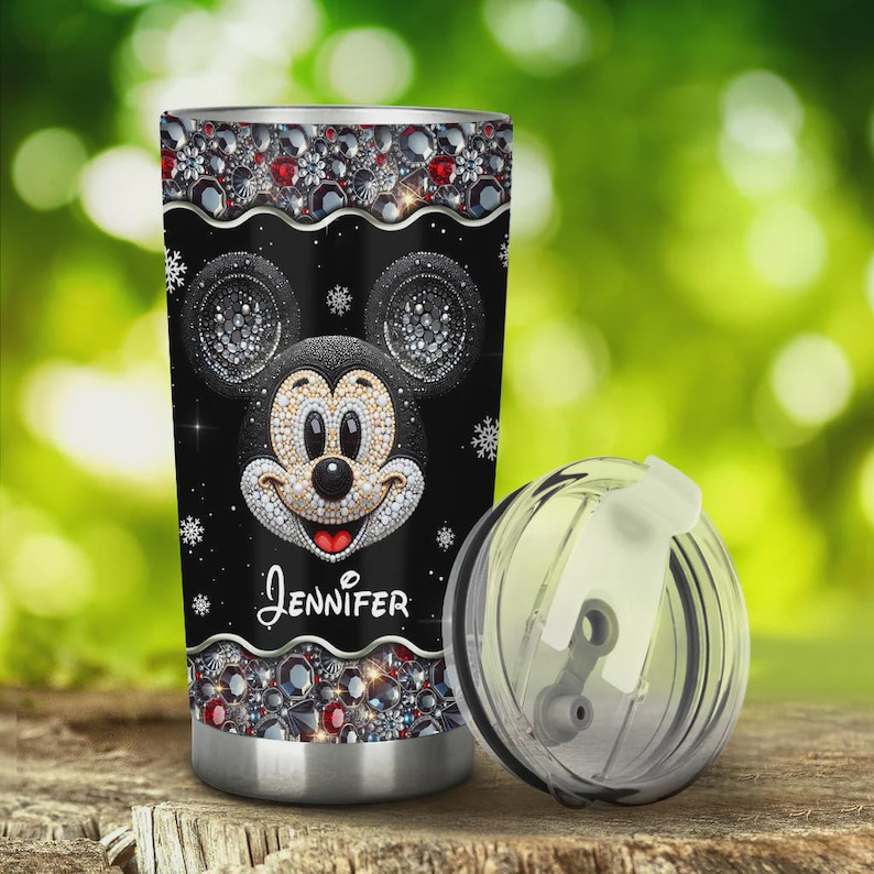 May include: Black tumbler featuring a sparkling Mickey Mouse design with the name "Jennifer" in cursive. The tumbler is adorned with jewel-like accents and snowflakes. Includes a clear lid.