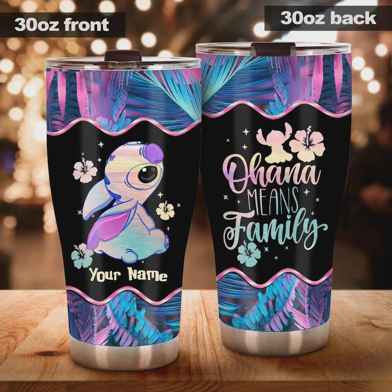 Op de afbeelding: Een 30oz roestvrijstalen beker met een zwarte achtergrond en een kleurrijk Stitch-ontwerp. De voorkant toont Stitch met de tekst "Your Name". De achterkant zegt "Ohana Means Family" met bloemaccenten. Het ontwerp bevat roze, blauwe en paarse tropische bladeren.