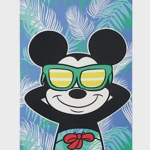 May include: Beach towel featuring Mickey Mouse wearing green sunglasses and a red bow tie. The background is a blue and green tropical leaf pattern. The towel is rectangular.