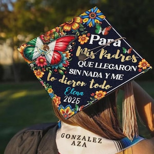 May include: A graduation cap with a dark blue background, adorned with colorful floral and butterfly designs. The cap features text in Spanish, including "Para Mis Padres" and "Elena 2025." A butterfly with the Mexican flag is prominently displayed.