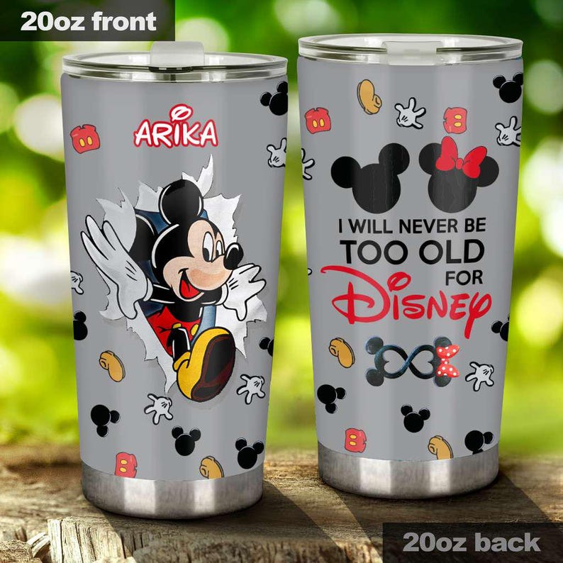 May include: A 20oz stainless steel travel mug with a grey background. One side features Mickey Mouse bursting through a torn paper effect, with the name "Arika" above. The other side says "I will never be too old for Disney".