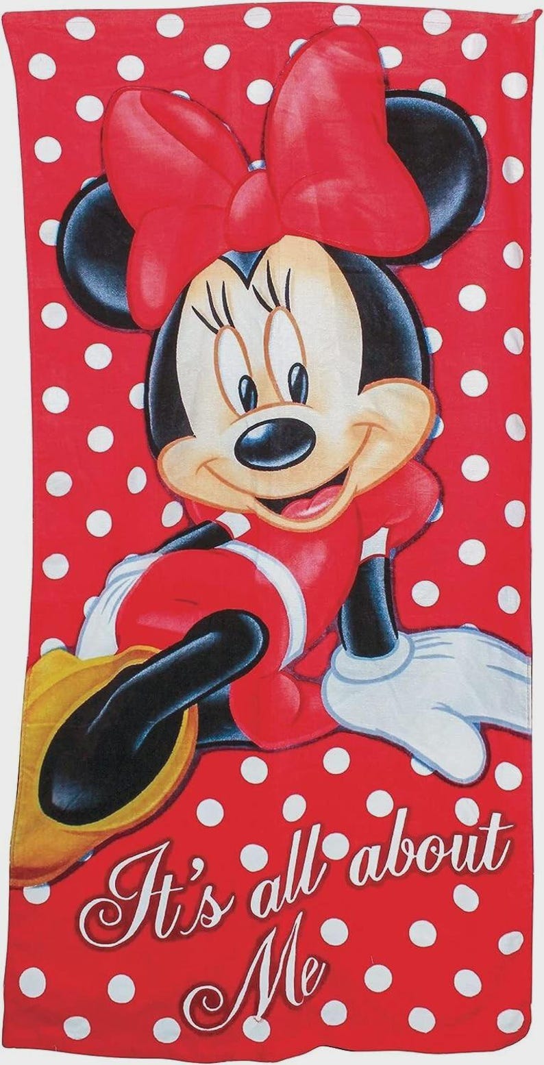 May include: A red and white polka dot beach towel featuring a smiling Minnie Mouse. Minnie is wearing a red dress, bow, and gloves. The towel has the text "It's all about Me".