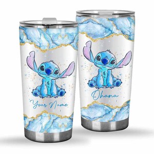 May include: Two stainless steel tumblers featuring a blue cartoon character with large ears. The tumblers have a white background with blue watercolor and gold glitter accents. One tumbler says "Your Name" and the other says "Ohana".