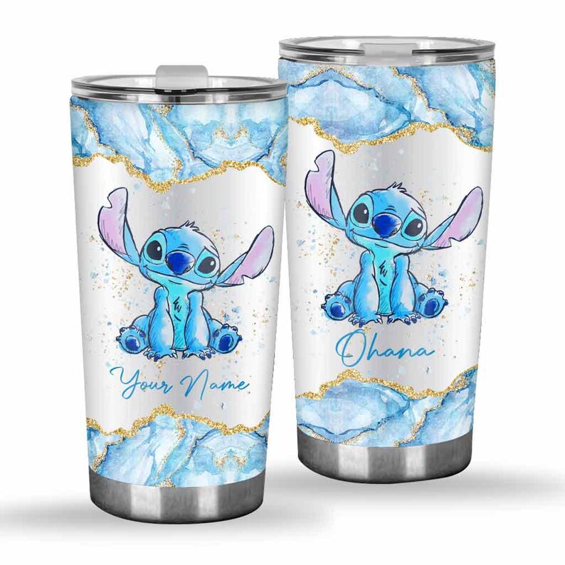 May include: Two stainless steel tumblers featuring a blue cartoon character with large ears. The tumblers have a white background with blue watercolor and gold glitter accents. One tumbler says "Your Name" and the other says "Ohana".