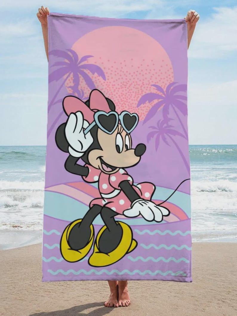May include: Beach towel featuring Minnie Mouse in sunglasses, a pink polka dot dress, and yellow shoes. The background includes a sunset, palm trees, and a wavy pattern in shades of purple, pink, and blue.