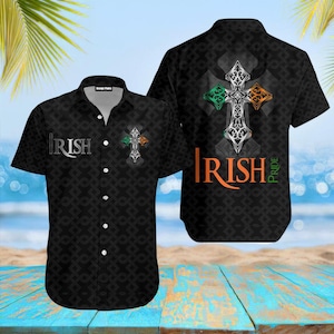 May include: Black short-sleeved button-down shirt with an Irish cross design. The shirt features the word "Irish" in white and orange, and the phrase "Irish Pride" in orange. The cross has green, white, and orange accents.