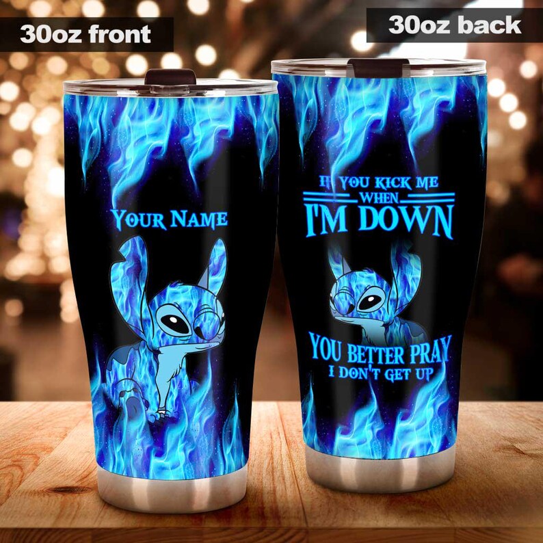 May include: A black 30oz tumbler featuring a blue cartoon character design with blue flames. The front of the tumbler has the text "YOUR NAME". The back of the tumbler has the text "IF YOU KICK ME WHEN I'M DOWN YOU BETTER PRAY I DON'T GET UP".