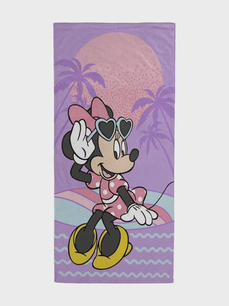 May include: A beach towel featuring Minnie Mouse in a pink polka-dot dress and heart-shaped sunglasses. The background includes a sunset, palm trees, and a wavy design in shades of purple, pink, and blue. The towel is rectangular.