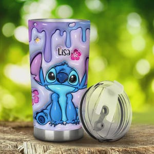Pode incluir: Um copo de a&ccedil;o inoxid&aacute;vel com um personagem de desenho animado, Stitch, em tons de azul. O copo tem uma tampa transparente e &eacute; decorado com um design gotejante roxo e azul, flores cor-de-rosa e o nome "Lisa".
