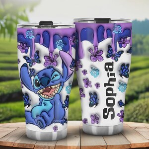 May include: Two stainless steel tumblers with a cartoon Stitch design. The tumblers feature a white background with purple dripping paint, butterflies, and flowers. One tumbler has the name "Sophia" printed vertically.