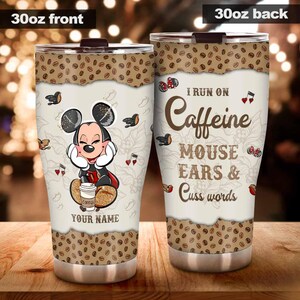 May include: A 30oz stainless steel tumbler with a brown lid. The front features a cartoon mouse with the text "YOUR NAME" and the back reads "I RUN ON Caffeine MOUSE EARS & Cuss words". The top and bottom have a coffee bean design.