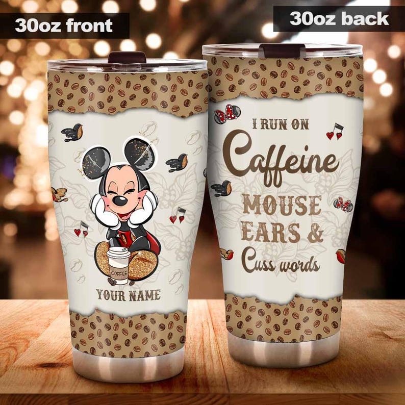 May include: A 30oz stainless steel tumbler with a brown lid. The front features a cartoon mouse with the text "YOUR NAME" and the back reads "I RUN ON Caffeine MOUSE EARS & Cuss words". The top and bottom have a coffee bean design.