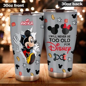 May include: A 30oz stainless steel tumbler with a grey background and a Mickey Mouse theme. The front features Mickey breaking through a torn paper effect, with the name "Arika". The back says "I will never be too old for Disney".