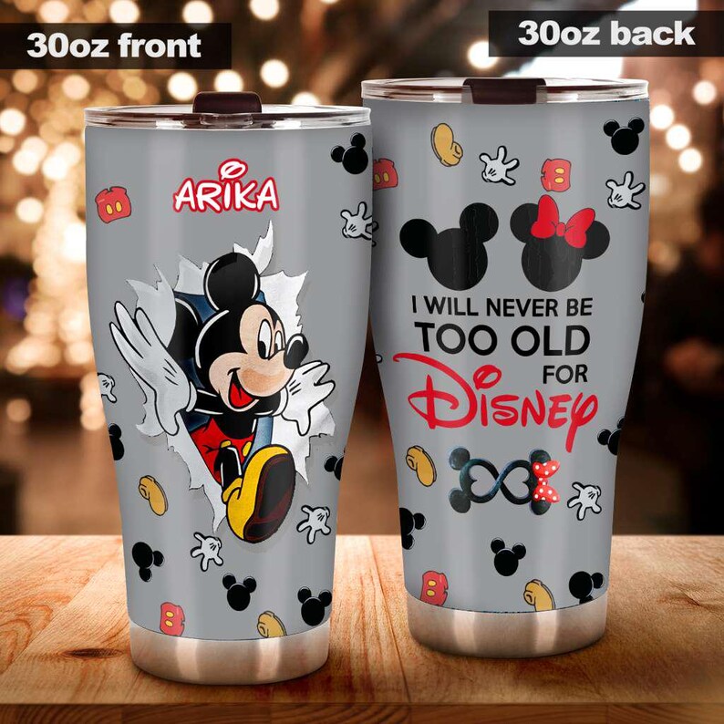 May include: A 30oz stainless steel tumbler with a grey background and a Mickey Mouse theme. The front features Mickey breaking through a torn paper effect, with the name "Arika". The back says "I will never be too old for Disney".