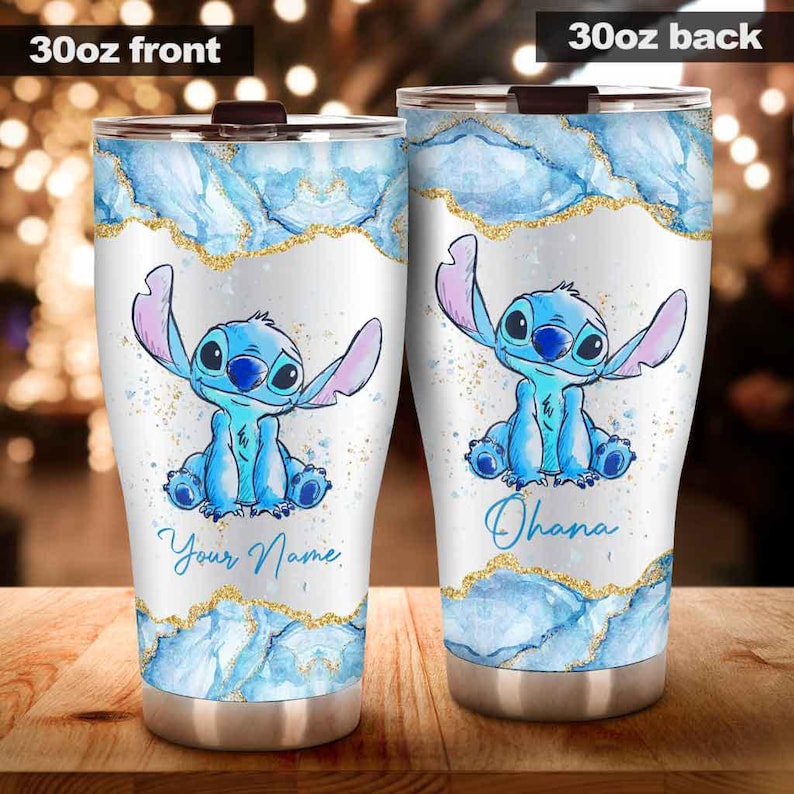 May include: A 30oz stainless steel tumbler featuring a blue cartoon character with large ears. The design includes blue watercolor-style accents, gold glitter, and the text "Your Name" on the front and "Ohana" on the back.