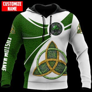 Puede incluir: Una sudadera con capucha blanca y verde con diseños de nudos celtas y el texto "CUSTOMIZE NAME" y "CUSTOM NAME". La sudadera con capucha presenta una capucha y cordones negros, con un gran diseño de nudo celta en la parte delantera.