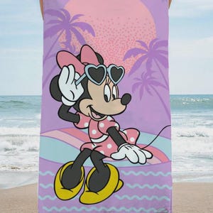 May include: Beach towel featuring Minnie Mouse in sunglasses, a pink polka dot dress, and yellow shoes. The background includes a sunset, palm trees, and a wavy pattern in shades of purple, pink, and blue.