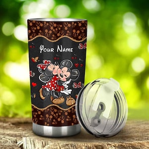 Puede incluir: Un vaso de acero inoxidable con un fondo negro que presenta a Mickey y Minnie Mouse abraz&aacute;ndose. El vaso tiene una parte superior marr&oacute;n con iconos de Mickey Mouse y las palabras "Your Name". Una tapa transparente est&aacute; al lado del vaso.