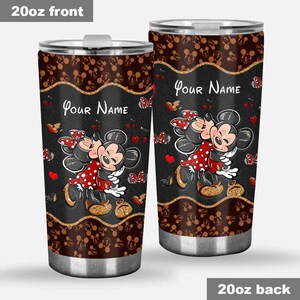 Puede incluir: Dos vasos de acero inoxidable de 20 oz con un dise&ntilde;o de Mickey y Minnie Mouse abraz&aacute;ndose. Los vasos tienen un fondo negro con un borde dorado, corazones rojos y mariposas. El texto "Your Name" est&aacute; impreso en la parte delantera.
