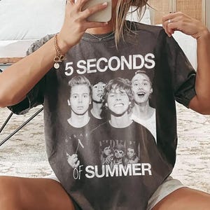 May include: Dark gray t-shirt featuring the text "5 SECONDS OF SUMMER" in white, with a graphic of five band members. The shirt is a vintage style, with a slightly faded appearance.