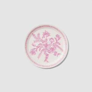 May include: A round paper plate with a floral design in pink. The plate features a central bouquet of flowers and foliage, surrounded by a decorative border. The plate is white with pink accents.