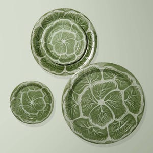 May include: Three round plates of varying sizes featuring a repeating green and white cabbage leaf pattern. The design displays detailed veining across the surface of each plate, with a consistent color palette of deep forest green and soft white.