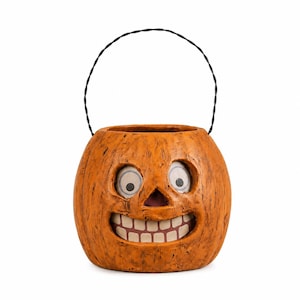 May include: A round orange pumpkin bucket with a textured surface, featuring a carved face with wide, circular eyes and a broad, toothy grin. The container includes a thin, black wire handle attached to the top for carrying purposes.