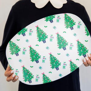 Pode incluir: Travessa oval branca com um padr&atilde;o repetido de &aacute;rvores de Natal verdes, la&ccedil;os vermelhos e ornamentos azuis e verdes. A travessa tem um tema festivo de feriado.