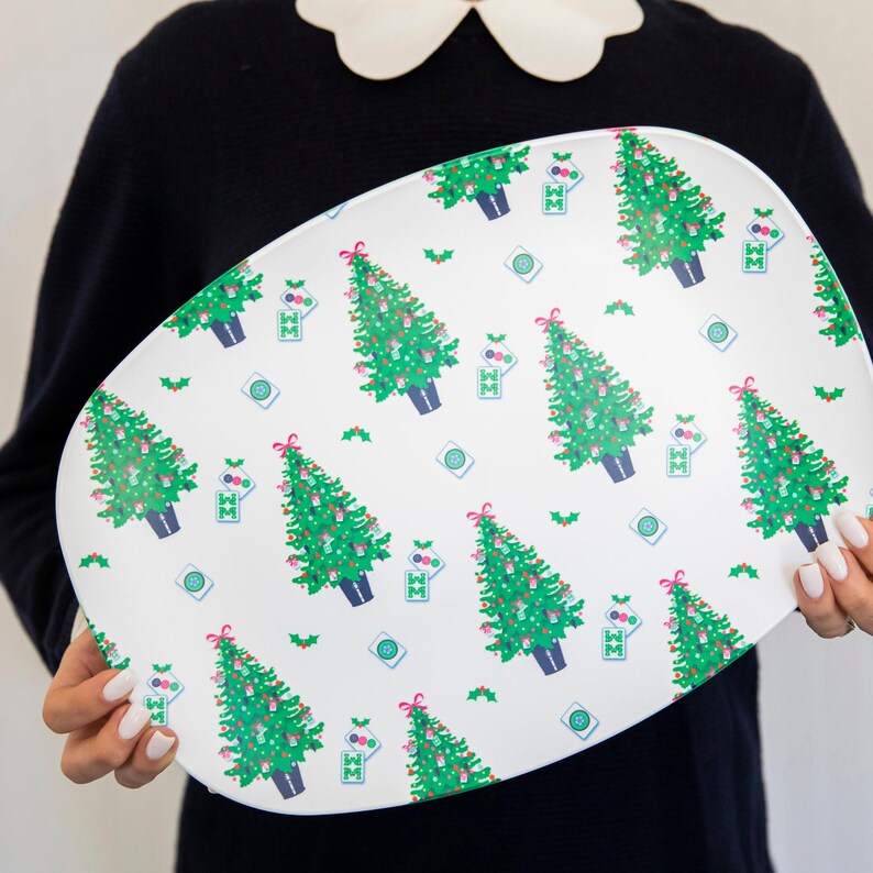 Pode incluir: Travessa oval branca com um padr&atilde;o repetido de &aacute;rvores de Natal verdes, la&ccedil;os vermelhos e ornamentos azuis e verdes. A travessa tem um tema festivo de feriado.