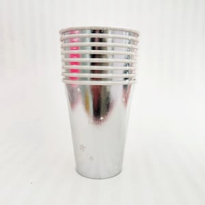 May include: A stack of silver paper cups with a metallic sheen and small star patterns. The cups have a white rim and are designed for beverages. Ideal for parties and celebrations.