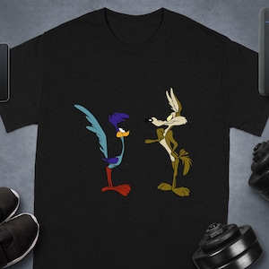 May include: Black t-shirt with a cartoon depiction of the Road Runner and Wile E. Coyote. The Road Runner is blue, purple, and red, and Wile E. Coyote is brown and tan. The tee shirt has a round neck.