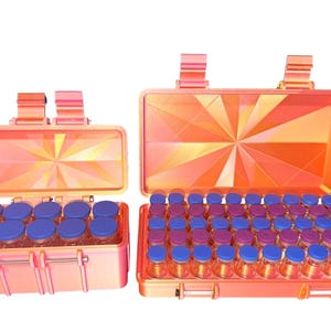 May include: Two open, peach-colored cases filled with small glass vials with blue lids. The cases have a geometric design on the inside and are set against a white background. The cases have handles.