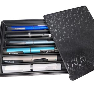 May include: A black rectangular storage case with a geometric patterned lid, containing six insulin pens in various colors including blue, black, grey, teal, and white. The pens are labeled with text including ConviPen and GensuPen2.