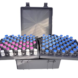 May include: A gray carrying case with two trays filled with small glass vials. The vials have blue, pink, and white caps. The case is open, revealing the vials arranged in rows. The case is designed for organization and transport.