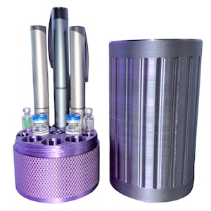 May include: A purple pen and vial holder with a textured base, holding pens and small glass vials with blue and green liquid. Next to it is a cylindrical container with vertical grooves. Both items are made of metal.