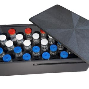 May include: A rectangular black storage box with a matching lid, containing multiple clear glass vials arranged in rows. The vials feature various colored caps, including white, blue, and red, secured within a black interior insert.
